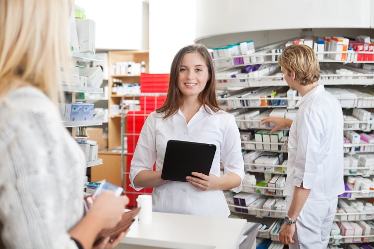 Portrait of female pharmacist holding tablet PC while attending customer on the counter