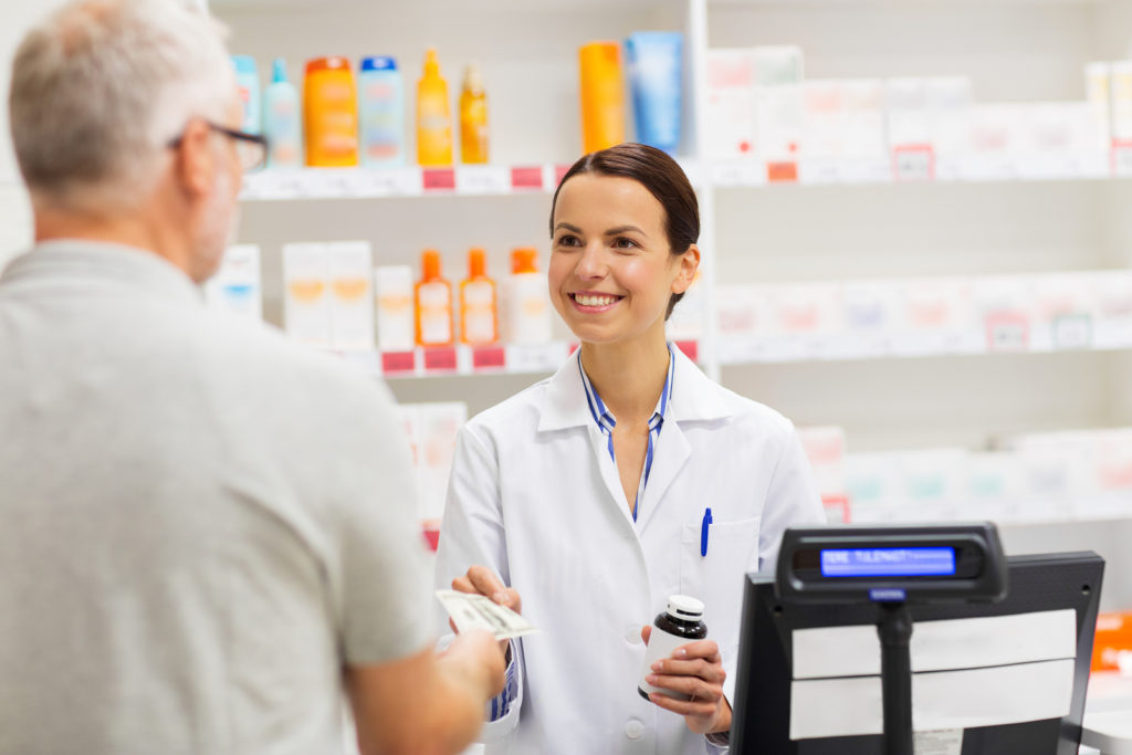 female pharmacist smiling and collecting payment from happy pharmacy customer at the checkout point of sale counter