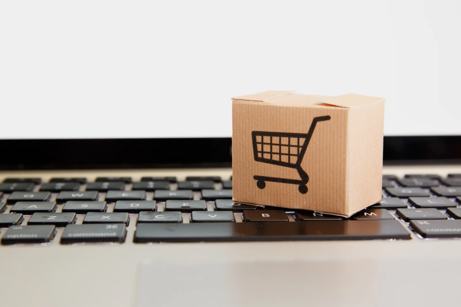 Online shopping . ecommerce and delivery service concept : Paper cartons with a cart or trolley logo on a laptop keyboard, depicts customers order things from retailer sites