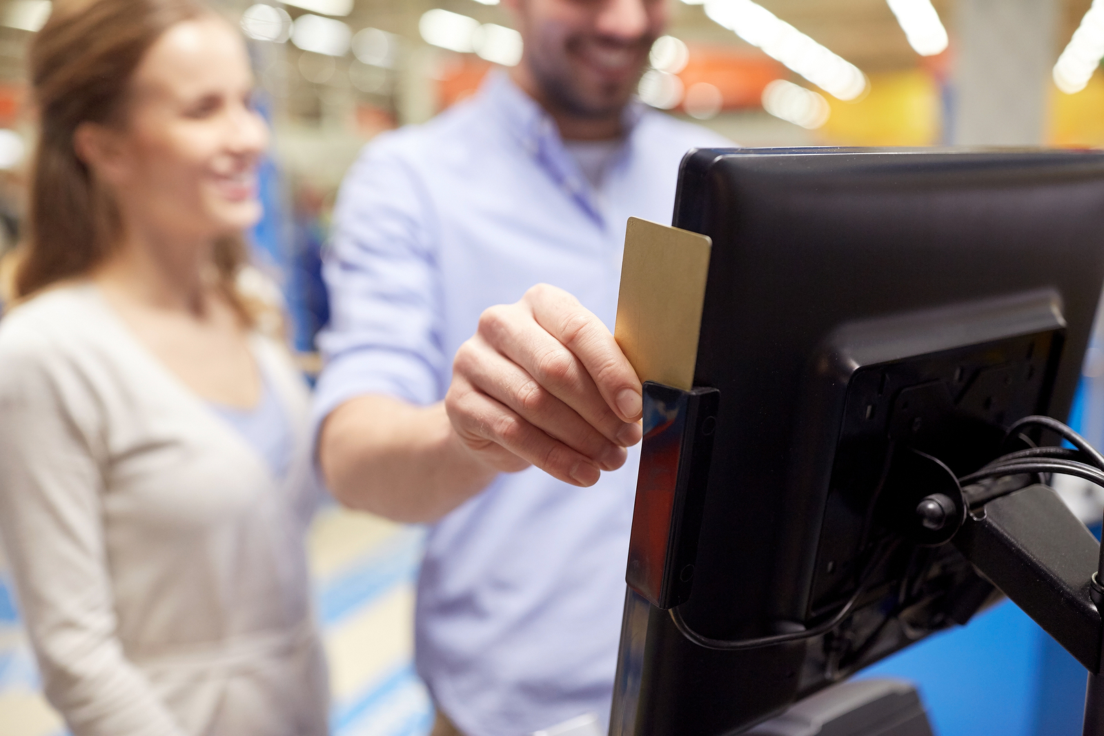 shopping, technology, consumerism and people concept - happy couple at grocery store or supermarket self-checkout swiping customer card