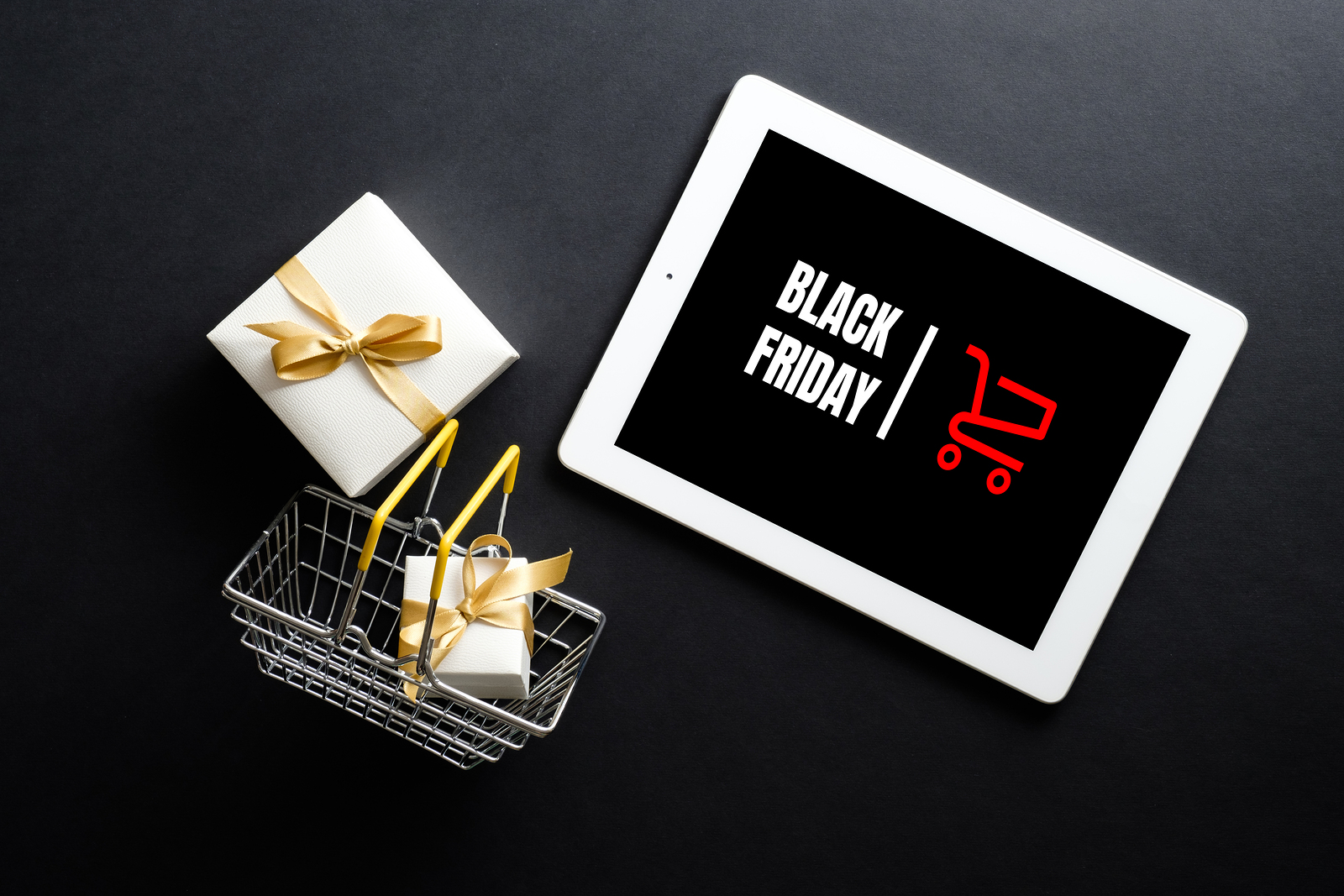 Black Friday sale concept. Tablet pad with sign "Black Friday" on screen, shopping basket, gift box over black background. Flat lay, top view, overhead.