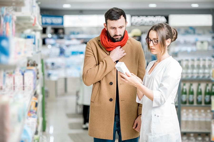Young woman pharmacist choosing medicine with male client dressed in coat and scarf in the pharmacy store