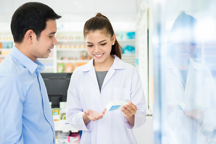 Female pharmacist holding medicine bottle giving advice to customer in chemist shop or pharmacy