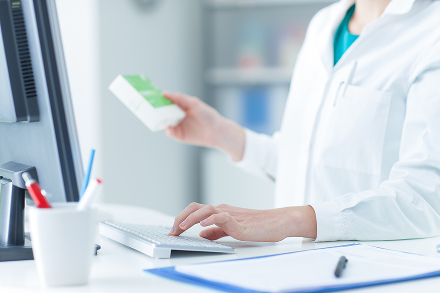 Pharmacist holding a medicine packet and searching that product in the computer database, healthcare and technology concept