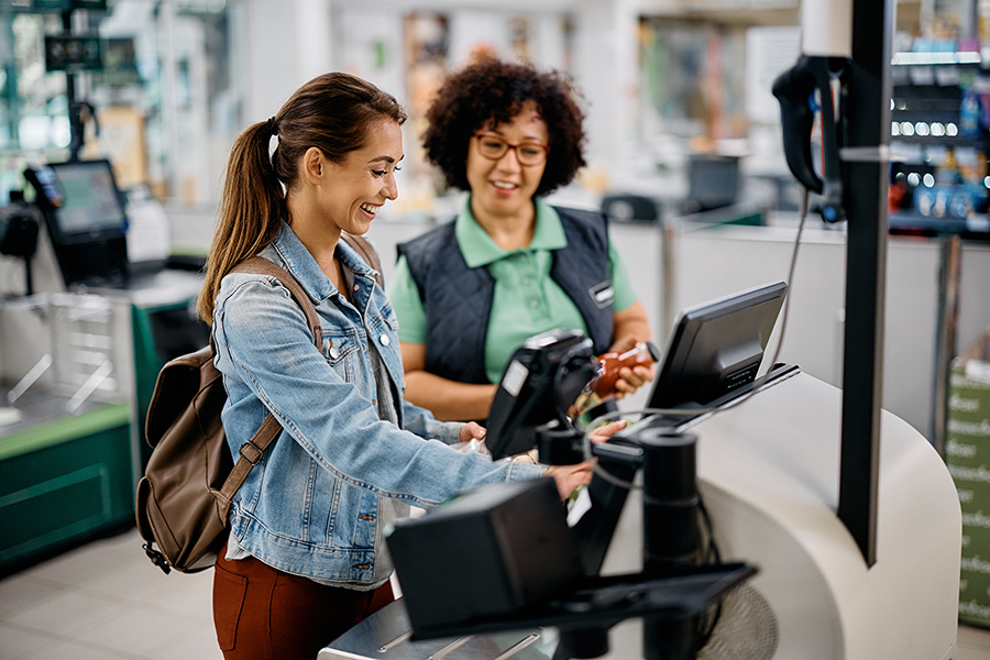 Young happy woman using self-service checkout with help of supermarket worker.