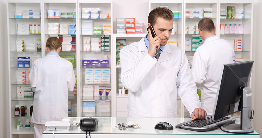 Pharmacist Man Talking on Mobile Phone while his Coworkers Worki