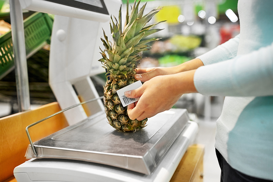 shopping, sale, consumerism and people concept - woman weighing pineapple on scale at grocery store