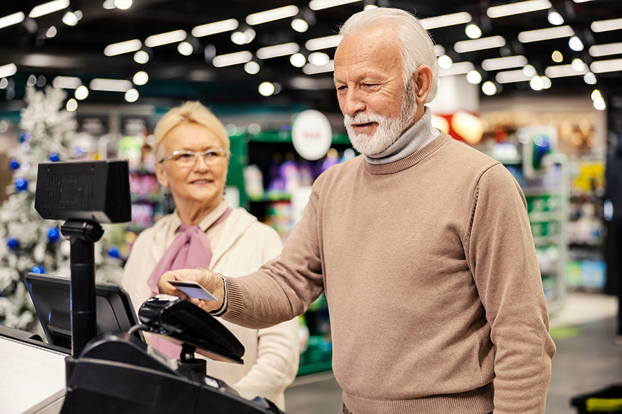 A senior man is paying with credit card on self-service cash register at the supermarket.