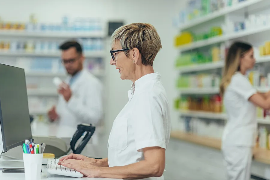 Senior female pharmacist working in a pharmacy with her young colleagues in the background