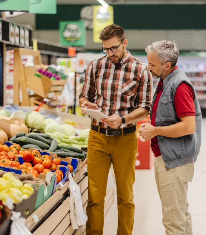 Two grocery store employees reviewing inventory data on a tablet in the produce section.