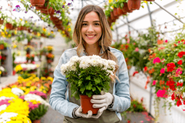 Smiling garden center employee holding a potted flower in a greenhouse, showcasing the benefits of a garden center POS system.