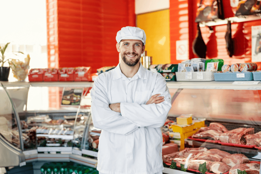 Butcher shop owner standing behind a fresh meat counter in a specialty food market.